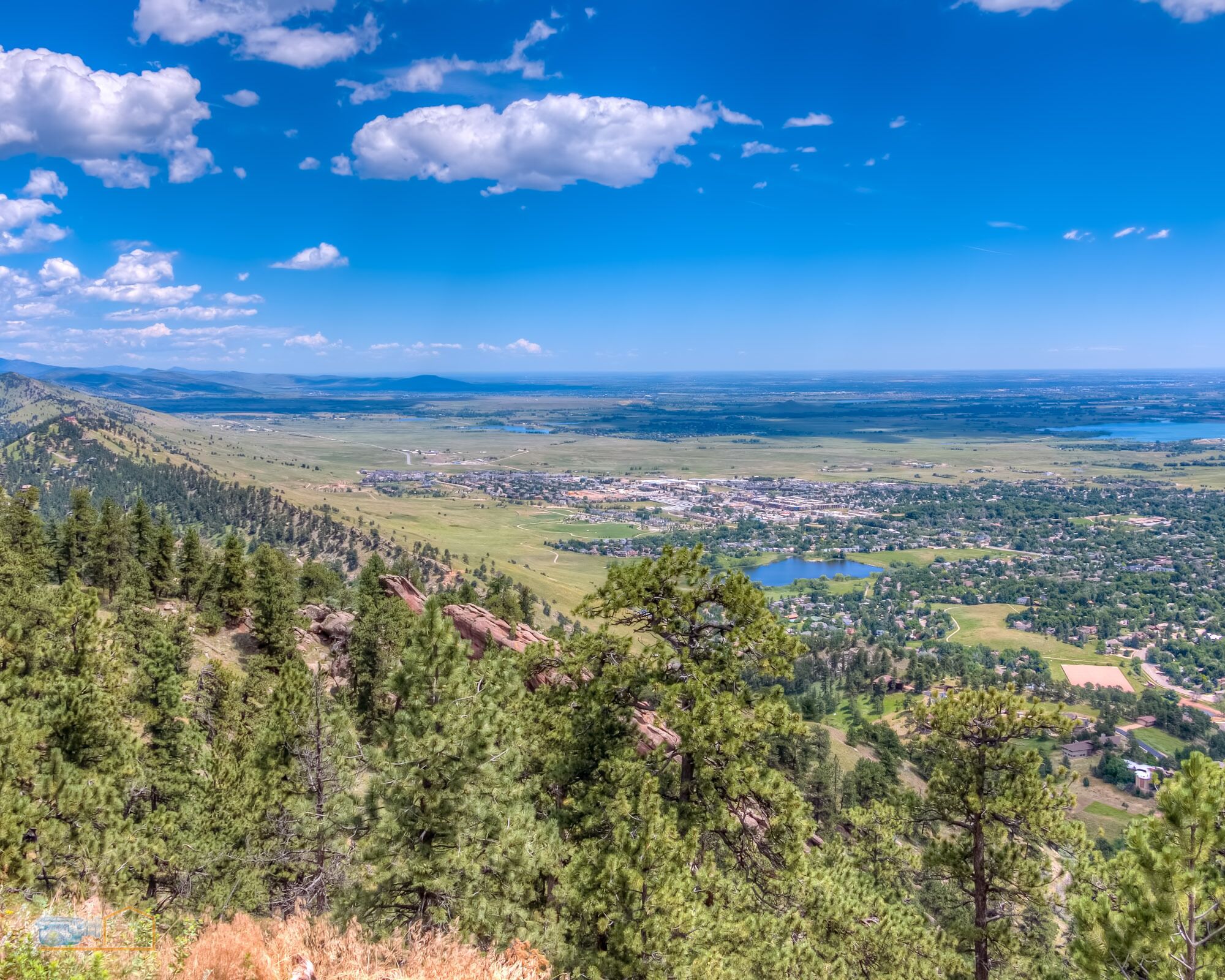 A panoramic view of a town surrounded by mountains and forests, with a clear sky.