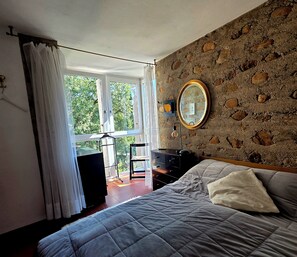Ein Schlafzimmer mit einem Bett, einem Schminktisch, einem Spiegel und Blick ins Freie.