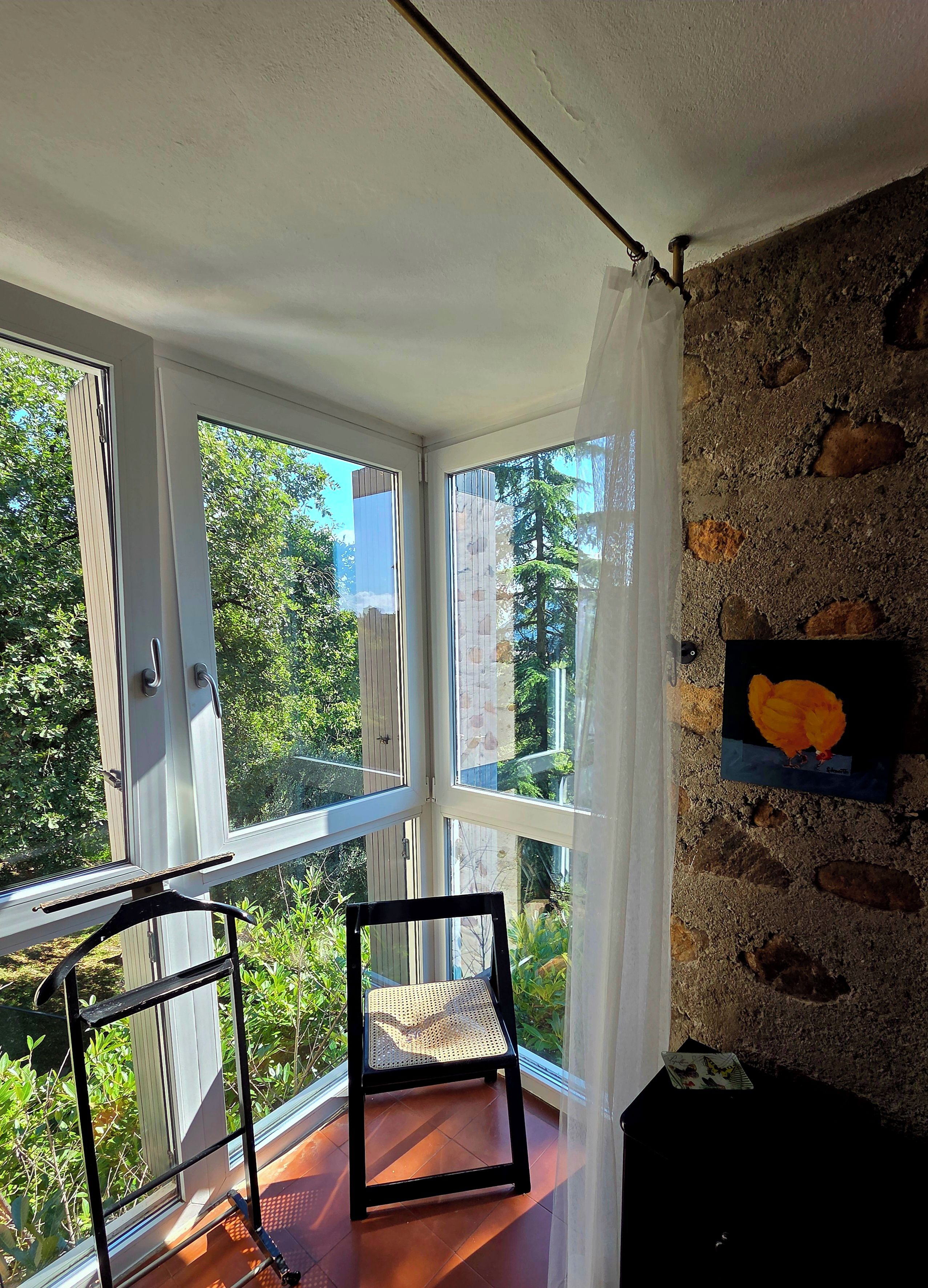 Een kamer met balkon, een stoel, een schilderij en uitzicht op groen.