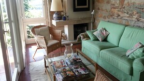 Ein gemütliches Wohnzimmer mit einem grünen Sofa, Korbstühlen, einem Glastisch mit Zeitschriften, einem Kamin und einer Steinwand mit Wandgemälde.