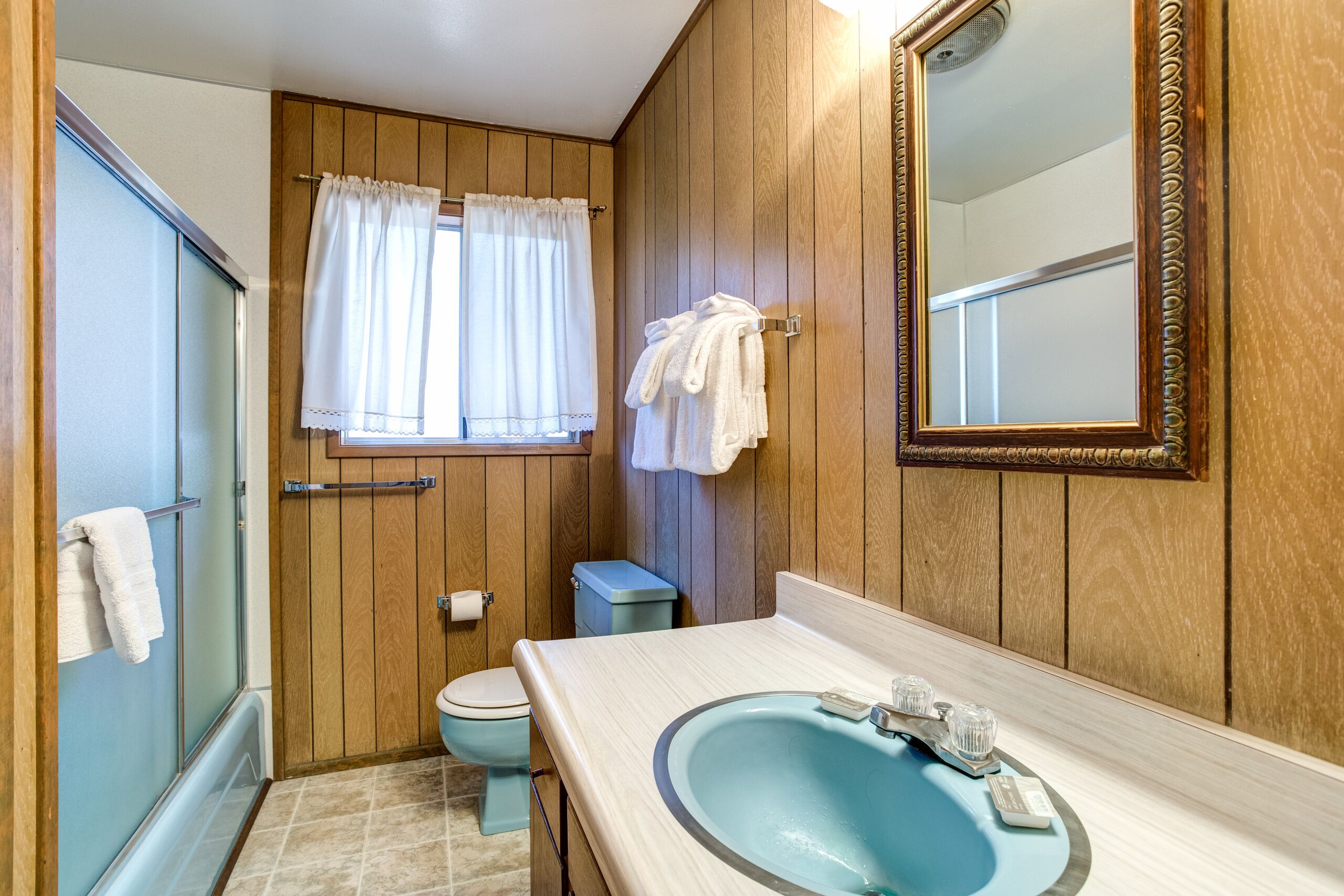 Un baño con pared de paneles de madera, un lavamanos azul, un inodoro y una zona de ducha.