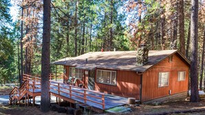 A rustic cabin with a wooden deck and a stone chimney.