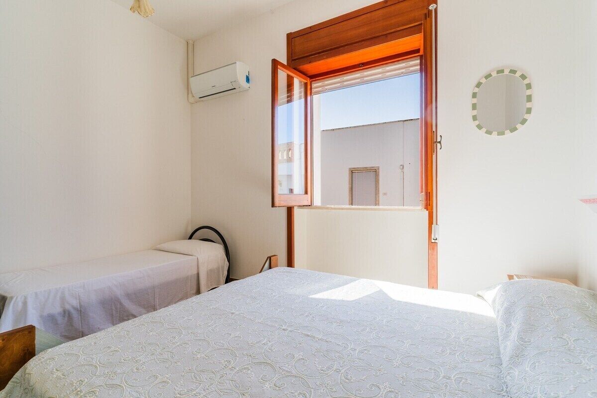Ein Schlafzimmer mit zwei Betten, einem Fenster, einer Klimaanlage und einem kleinen Balkon.