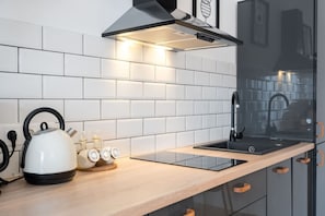 A modern kitchen with a stainless steel range hood, a black faucet, and a white kettle on the counter. - Esiko by MRG Apartments | Balcony | University Square | Old Town | City Centre (București)