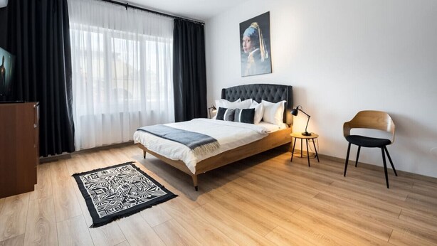 A modern bedroom with a large bed, a bedside table, a chair, and a painting on the wall. - Esiko by MRG Apartments | Balcony | University Square | Old Town | City Centre (București)