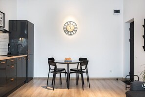 Een moderne keuken met een eethoek, met een ronde tafel met stoelen, een wandklok en een zwarte koelkast.