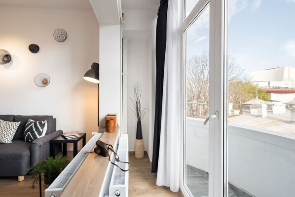 A modern living room with a sofa, a radiator, a small table, and a window with a view of buildings.