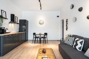 A modern kitchen with a dining area, a sofa with patterned cushions, and a wall clock. - Esiko by MRG Apartments | Balcony | University Square | Old Town | City Centre (București)