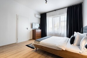 A bedroom with a bed, a television, a dresser, and a window with curtains. - Esiko by MRG Apartments | Balcony | University Square | Old Town | City Centre (București)