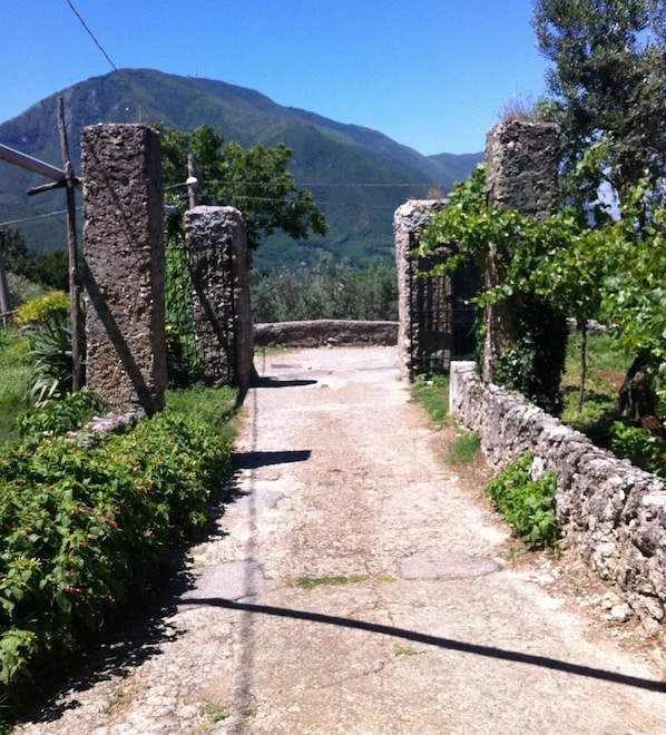 A narrow, unpaved path leading through a rustic stone structure with a mountainous backdrop.