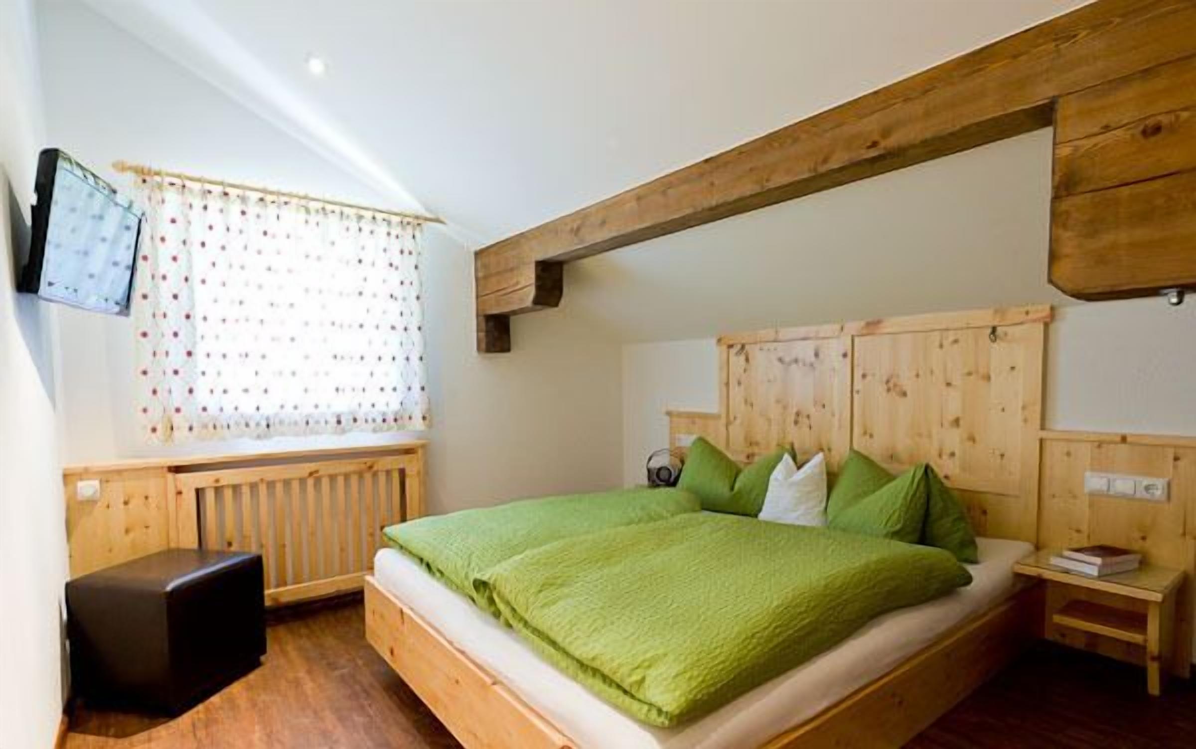 A bedroom with a wooden headboard, a bed with green bedding, a small bedside table, and a radiator.