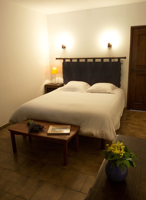 A neatly made bed with a headboard, a bedside table with a book and a bouquet of flowers, and a lamp on a nightstand. - Facing a green esplanade, Lardiers cottage for 5 people (Forcalquier)
