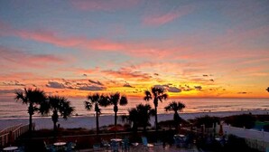 Ein Sonnenuntergangsblick von einer Strandlage mit Palmen und einer Terrasse mit Stühlen und Tischen.