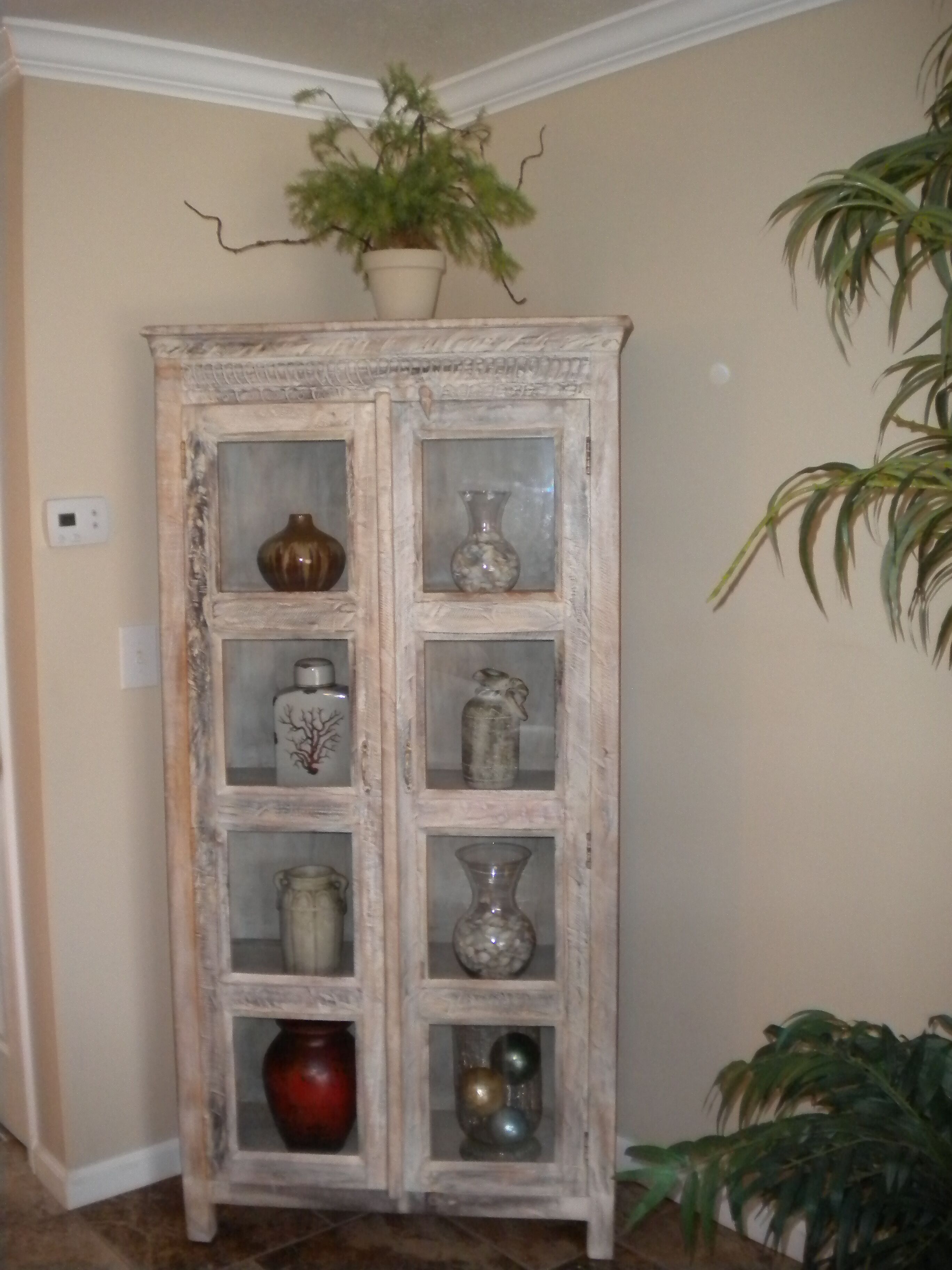 A tall, rustic cabinet with multiple glass doors, each containing various decorative items.