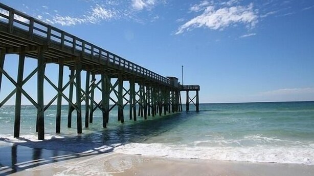 Eine Pier, die sich ins Meer erstreckt, mit blauem Himmel darüber.