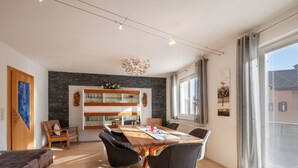Un comedor moderno con una mesa y sillas de madera, un aparador de vidrio con vajilla, y vistas al exterior a través de amplias ventanas.