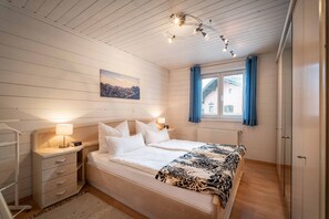 A bedroom with a bed, bedside tables, a lamp, a window with curtains, and a painting on the wall.