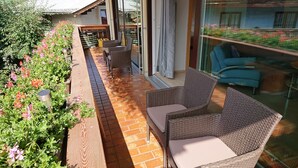 Un patio iluminado por el sol con mobiliario de mimbre, suelo de ladrillo y vistas a un jardín lleno de flores.