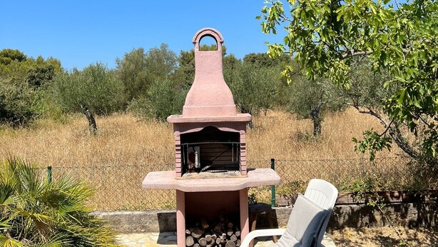 Area barbecue esterna in pietra con griglia, una poltrona da relax e un vialetto in pietra.