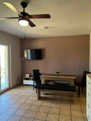 Ein Essbereich mit Holztisch und -stühlen, einem Deckenventilator und einem an der Wand befestigten Flachbildfernseher.
