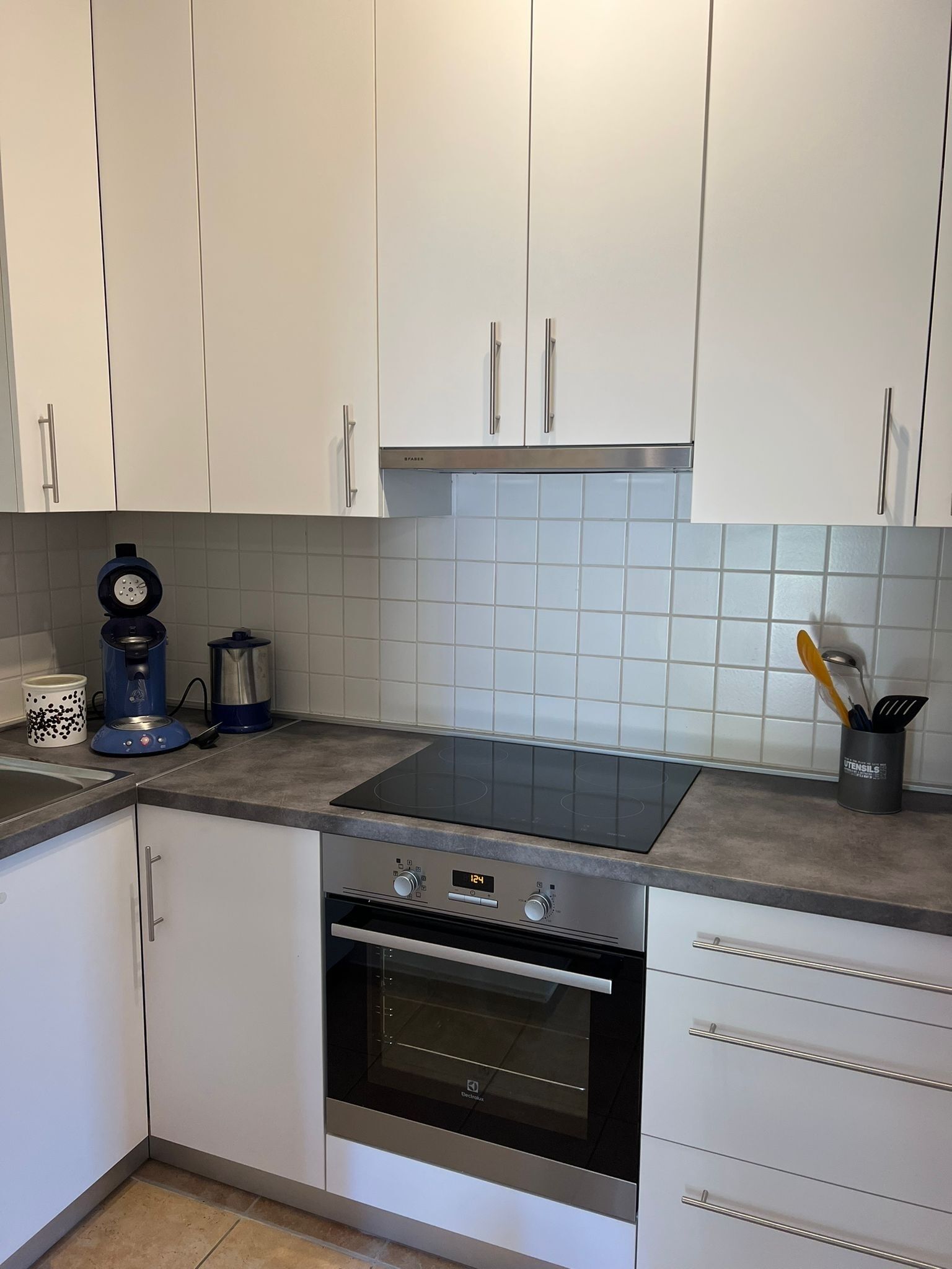 Een keuken met witte kasten, een zwarte oven, een kookplaat en een koffiezetapparaat.