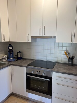 Eine Küche mit weißen Schränken, einem schwarzen Backofen, einem Kochfeld und einer Kaffeemaschine.