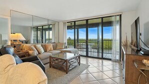 Amplia sala de estar con un sofá grande, una mesa de centro y un televisor. La habitación tiene un balcón con vistas al exterior.