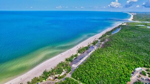Vista aérea de una zona costera con playa, aparcamiento y vegetación densa.