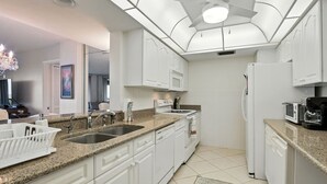Una cocina moderna con armarios blancos, encimeras de granito, un microondas integrado y un ventilador de techo.