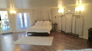 Un dormitorio con cama, mesita de noche, una silla y un ventanal con cortinas.
