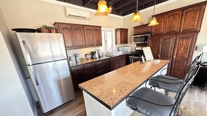 Una cocina moderna con armarios de madera oscura, electrodomésticos de acero inoxidable, encimera de granito e iluminación colgante.