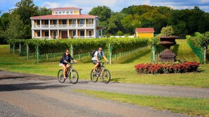 Two cyclists on a gravel path with a large yellow building in the background, surrounded by greenery and a well-maintained garden.