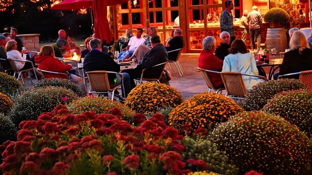 An outdoor dining area with people seated at tables, surrounded by vibrant flower beds.