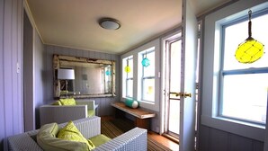 A room with wicker furniture, a mirror, a bench, and a window with a hanging light fixture.