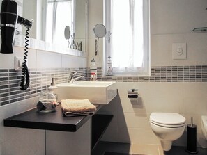 Une salle de bain moderne équipée d’un lavabo, d’un miroir, de toilettes et d’un sèche-cheveux.