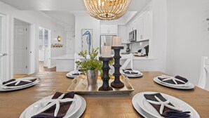 Una cocina moderna con armarios blancos, una lámpara de araña y una mesa de comedor con platos y servilletas.