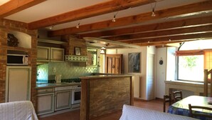 Uma cozinha acolhedora com vigas de madeira aparentes, uma ilha de pedra e um espaço de refeições com mesa e cadeiras.