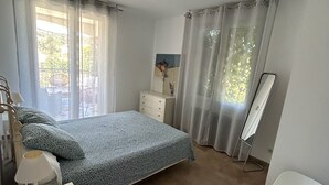 A bedroom with a bed, a bedside table, a dresser, a mirror, and a chair.