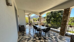 A covered patio with a mosaic floor, stone pillars, and a table with chairs.