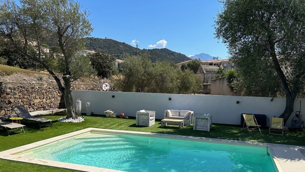 A rectangular swimming pool with a surrounding grassy area, outdoor furniture, and a stone wall.