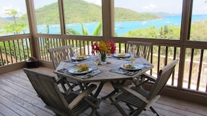 A wooden deck with a table set for dining, overlooking a bay with boats.