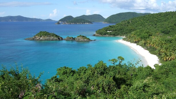A coastal landscape with a beach, clear blue waters, and lush greenery.