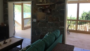 A room with a stone wall, a green sofa, and a view of a beach through a glass door.