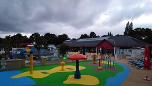 A playground with colorful play structures and a building with a red roof in the background. - 3 Bedroom mobile home Siblu Domaine de Kerlann  Brittany France 131 (Pont-Aven)