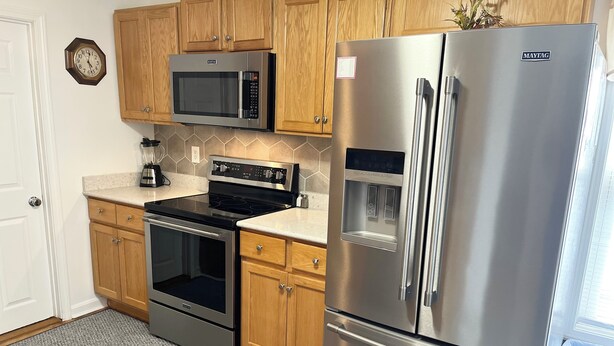 A kitchen with wooden cabinets, a stainless steel refrigerator, a microwave, a stove, and a water dispenser. - One Bedroom Apartment with Separate Bunk Bed Area (Shrewsbury)