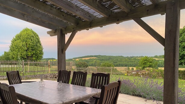 A covered outdoor dining area with a table and chairs, overlooking a scenic landscape with hills and a wooden fence. - Traditional French farmhouse for 10 guests, private pool, stunning country views (Montboyer)