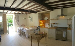 A dining area with a table set for four, a kitchen with a stove and oven, and a brick wall. - French farmhouse Gite for up to 10 guests, private pool, stunning country views (Montboyer)