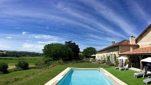 A swimming pool with a view of a rural landscape, a stone building with a tiled roof, and a grassy area with lounge chairs. - Traditional French farmhouse for 10 guests, private pool, stunning country views (Montboyer)