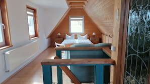 Une chambre avec un plafond en pente, des murs en bois, un lit avec une literie blanche, une table de chevet et une fenêtre.
