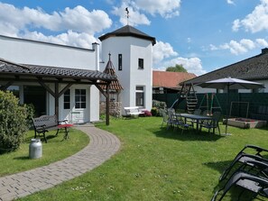 Une cour avec un bâtiment blanc, un patio couvert et une balançoire.